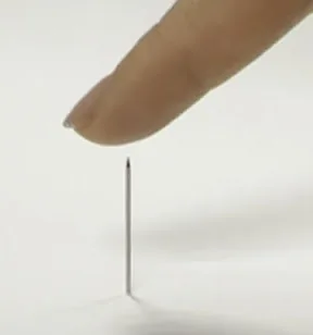 A needle held just above a fingertip, illustrating pricking.